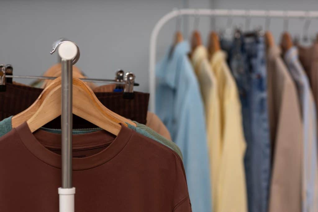 Clothes neatly hung on wooden hangers in a wardrobe rack, with shirts and jeans arranged in the background.